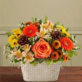 Mixed bouquet in a patterned white metal container with orange and yellow flowers