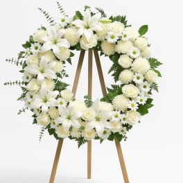 White floral wreath on a wooden easel with roses and lilies