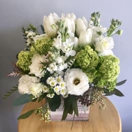 White and green floral arrangement with tulips, lisianthus, and daisies in a rustic wooden cube vase