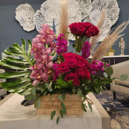 Large floral arrangement with red roses, pink orchids, and pampas grass in a wooden box