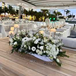 White floral centerpiece on a wooden table at an outdoor dining setup