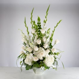 Tall white arrangement of roses, hydrangeas, and accent blooms in a white ceramic vase