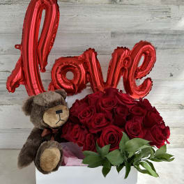 Red roses in a white box with a teddy bear and red "Love" balloon