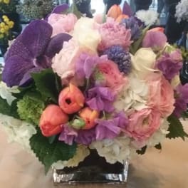 Mixed bouquet of pink, purple, and white flowers in a square glass vase