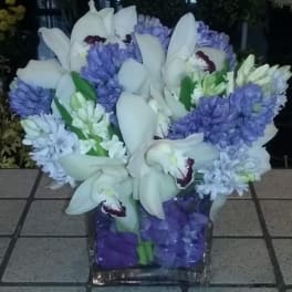 White orchids and purple flowers arranged in a square glass vase