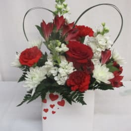 Red and white floral arrangement in a white heart-decorated container