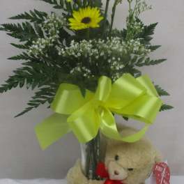 Yellow daisy bouquet in a glass vase with a teddy bear