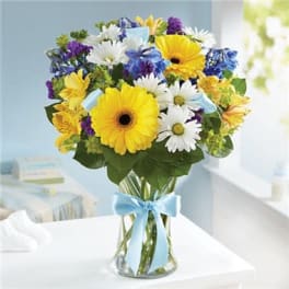 Bouquet of yellow gerbera daisies, white daisies, and blue flowers in a glass vase