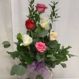 Bouquet of multicolored roses in a clear glass vase with a purple ribbon