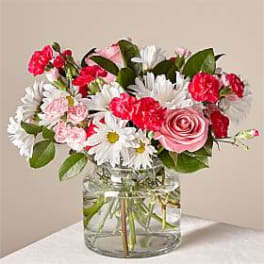 Pink roses, red carnations, and white daisies in a clear glass vase