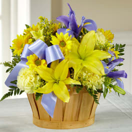 Yellow lilies and daisies in a wooden basket with a lavender ribbon