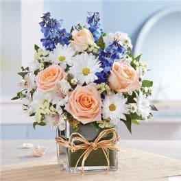 Bouquet of peach roses, white daisies, and blue flowers in a glass vase