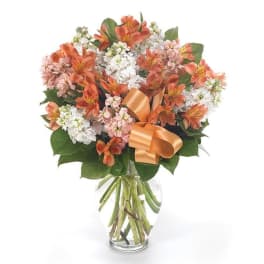 Bouquet of orange and white flowers in a clear glass vase with a ribbon