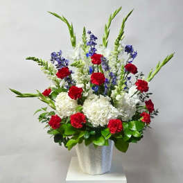 Tall floral arrangement with red, white, and blue flowers in a white vase