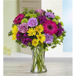 Mixed bouquet of purple, pink, and yellow flowers in a clear glass vase