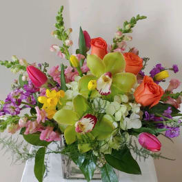 Mixed bouquet with orange roses, green orchids, and pink tulips in a glass vase