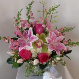 Pink lilies and roses arranged in a glass vase with a small white bird figurine