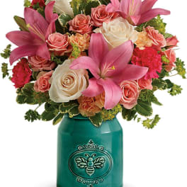 Pink lilies and roses arranged in a teal vase with a bee design