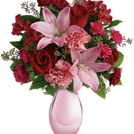 Pink lilies and red roses arranged in a pink glass vase