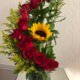 Arrangement of red roses and a yellow sunflower in a green glass vase