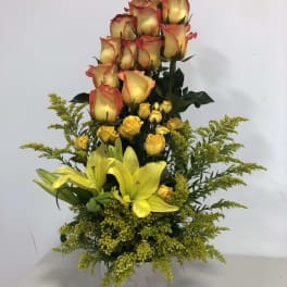 Tall arrangement of yellow lilies and yellow-red roses in a square vase