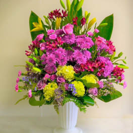 Tall arrangement of pink flowers, yellow hydrangeas and lilies in a white pedestal vase
