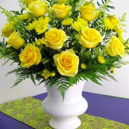 Arrangement of yellow roses and yellow daisies in a white urn vase on a purple table