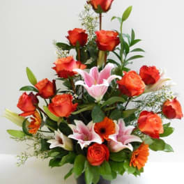 Tall arrangement of orange roses, pink lilies, and orange gerbera daisies in a black vase
