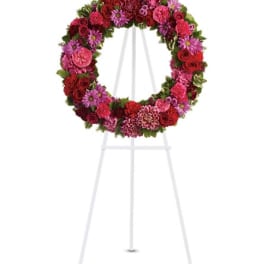 Circular floral wreath on a white easel with red and pink blooms