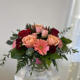 Bouquet of peach and red roses with a pink gerbera daisy in a glass vase