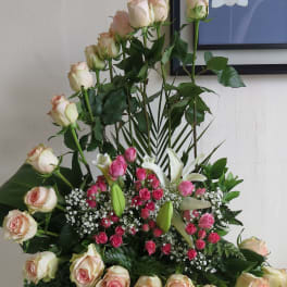Tall arrangement of cream and pink roses with white lilies and small pink roses in a curved design