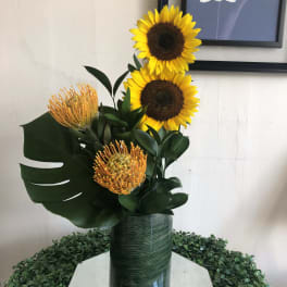 Sunflowers and orange pincushion protea in a tall green vase