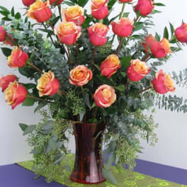 Tall arrangement of pink and yellow roses with lush foliage in a red glass vase