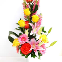 Tall bouquet of roses, lilies, and pink flowers in a white vase