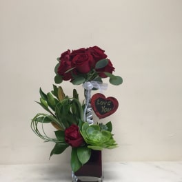 Vertical arrangement of red roses and a green succulent in a glass vase with a heart pick reading Love You.