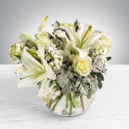 Arrangement of white lilies and roses with gray foliage in a round glass vase
