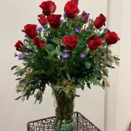 Red roses arranged in a clear glass vase with purple filler flowers