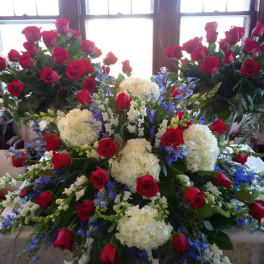 Large floral arrangement of red roses, white hydrangeas, and blue flowers