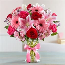 Pink and red mixed bouquet in a clear glass vase with a pink ribbon.
