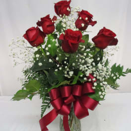 Red roses in a glass vase with baby's breath and a red ribbon
