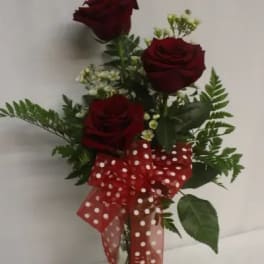 Three red roses in a glass vase with a red polka-dot bow