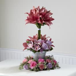 Tall pink floral arrangement in a silver container with a low ring of roses