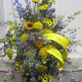Tall standing floral spray with yellow and blue flowers on a black easel