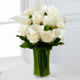 White roses and calla lilies arranged in a clear glass vase.