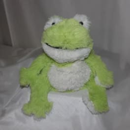 Green and white plush frog toy sitting on a bed
