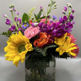 Colorful bouquet with sunflowers, roses, and purple blooms in a glass vase