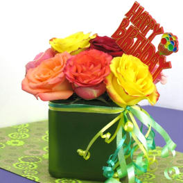 Bright mixed roses in a green cube vase with a Happy Birthday sign and curling ribbons.