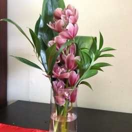 Pink orchids arranged in a clear glass vase with broad green leaves