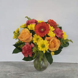 Bright bouquet of orange roses, red gerberas, yellow daisies, and carnations in a glass vase