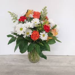Mixed bouquet of orange roses, red carnations, and white daisies in a clear glass vase